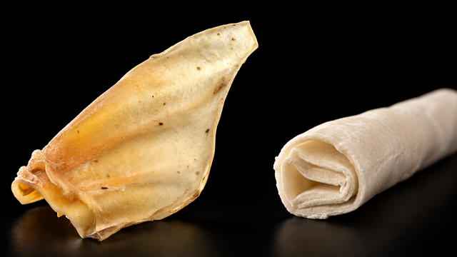 A natural dried cow ear and a rolled rawhide chew show different material structures.