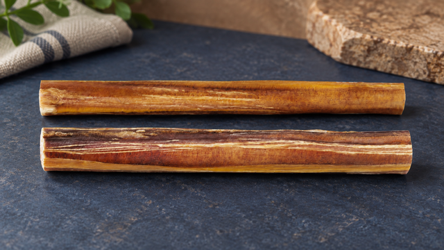 Standard and jumbo bully sticks of the same length lie side by side to compare thickness.